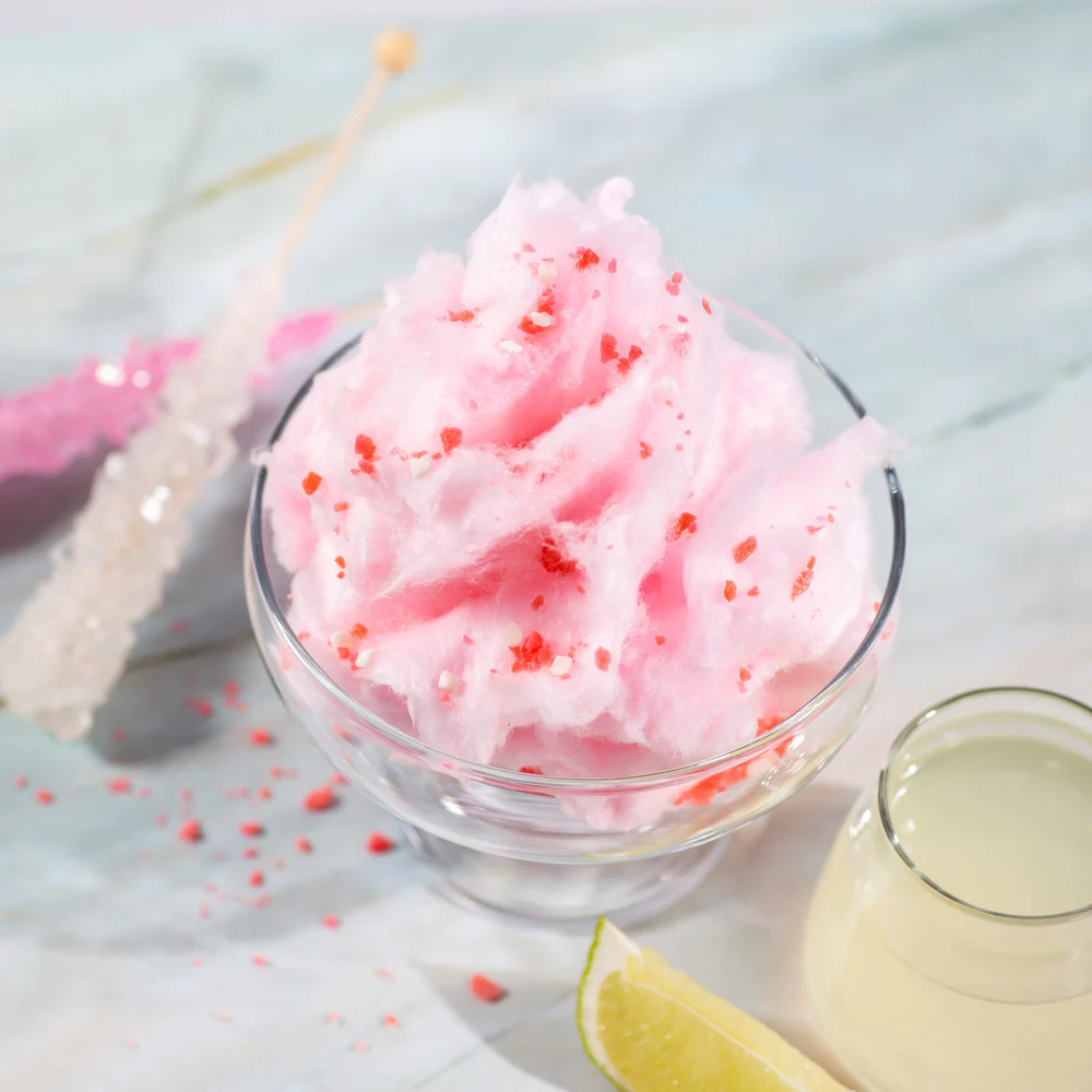 Cotton candy margarita in a glass with pink cotton candy on top and pink sugar rim