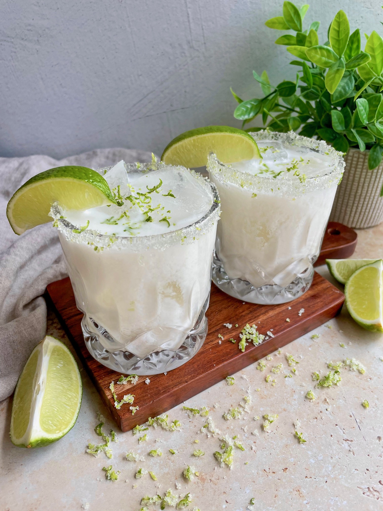 Coconut lime margarita on a wooden board with lime wedges and toasted coconut