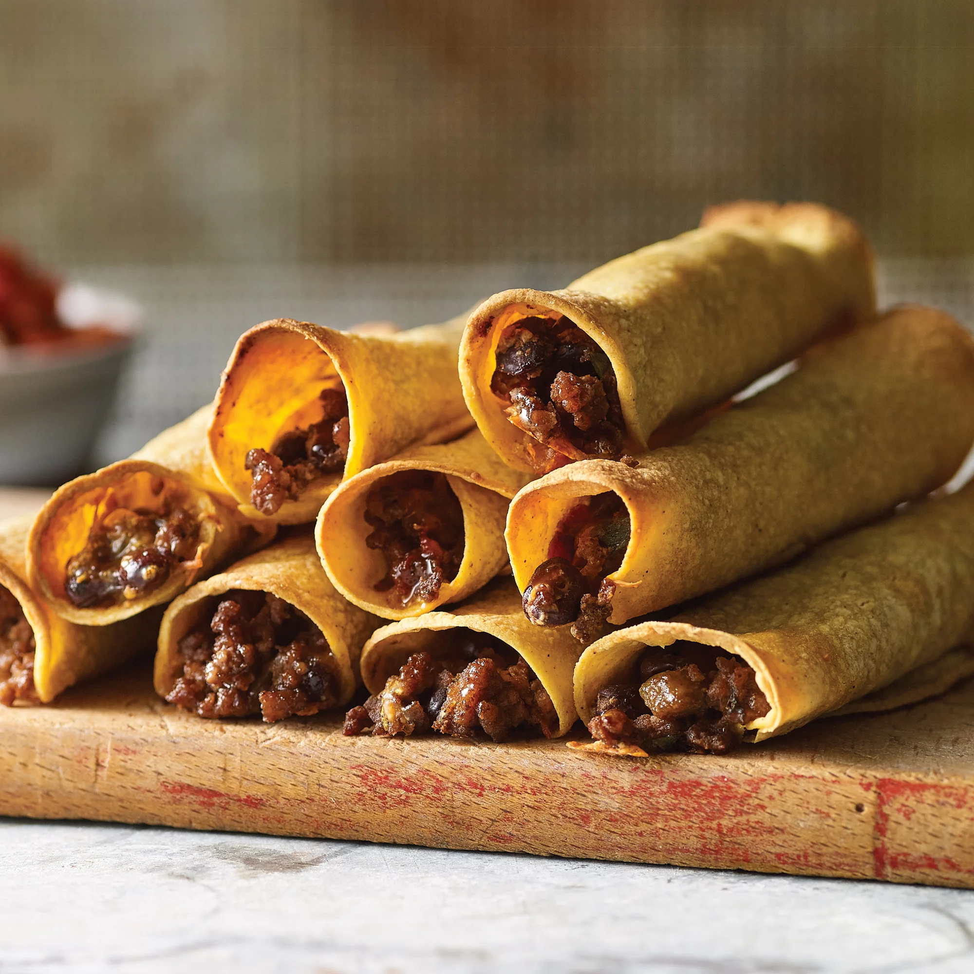 Crispy baked beef taquitos lined up on a plate with salsa and sour cream for dipping