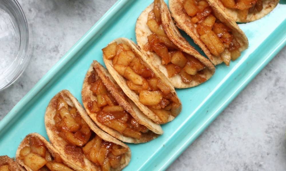 Apple pie tacos with cinnamon sugar shells and caramel drizzle on a wooden board