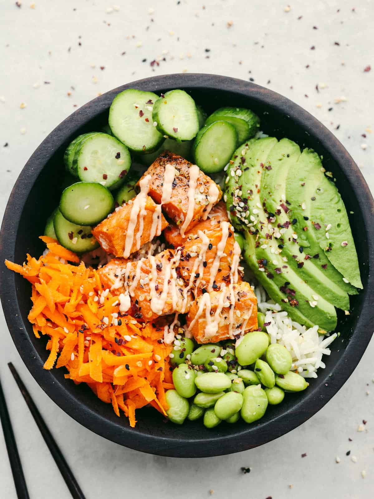 Healthy salmon rice bowls with avocado cucumber edamame and spicy sauce